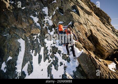 Vue arrière des grimpeurs avec sacs à dos à l'aide d'une corde fixe tout en montant haute montagne rocheuse. Hommes alpinistes escalade formation naturelle de roche Banque D'Images