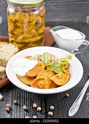 Safran de champignons salés à la crème aigre, feuille de cassis et branche d'aneth dans une assiette, fourchette, serviette et pain sur fond de bois Banque D'Images