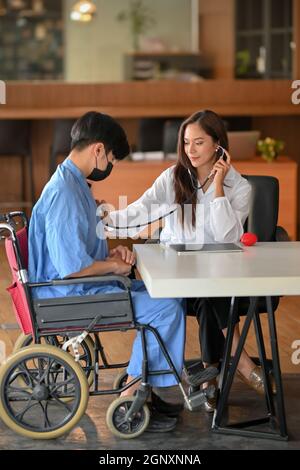 Un jeune médecin asiatique tient le stéthoscope pour vérifier l'examen de la fréquence cardiaque du patient handicapé dans le centre de santé Banque D'Images
