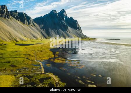 Vue aérienne de la scène stupéfiante du cap Stokksnes avec Vestahorn. Vue panoramique islandaise des dunes de sable noir par marée avec de l'herbe jaune Banque D'Images