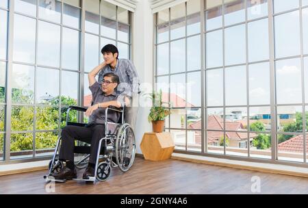 Un homme d'affaires asiatique âgé en fauteuil roulant discute de l'interaction avec l'équipe du bureau. Le vieil homme en fauteuil roulant et son jeune homme Banque D'Images