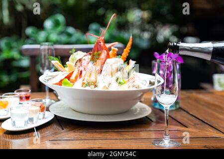 Un serveur verse du vin blanc dans un verre de vin et sert au client dans un restaurant avec un grand bol de fruits de mer sur glace en arrière-plan. Restaurant gastronomie Banque D'Images