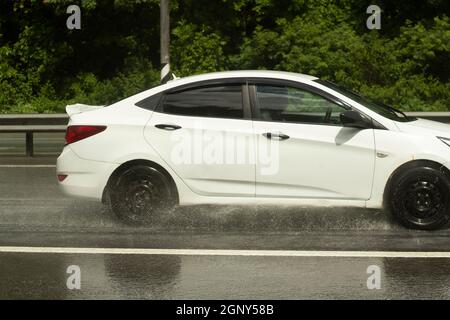 La voiture roule sur une route humide. Route glissante après la pluie. Éclaboussures sous les roues de transport. Pluie sur l'autoroute. L'été en baisse dans les s. Banque D'Images