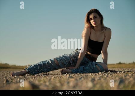 grave triste fille de tramp en jeans déchirés est assis sur une route déserte Banque D'Images