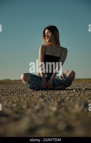 grave triste fille de tramp en jeans déchirés est assis sur une route déserte Banque D'Images