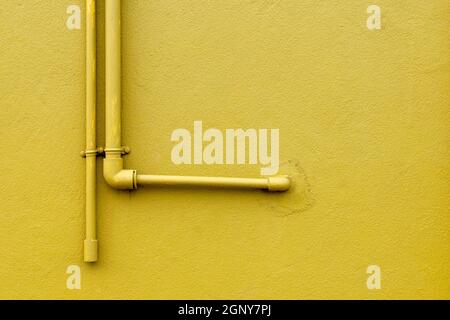 Raccord de tuyaux en plastique en forme de L fixé sur un mur en béton de couleur jaune. Banque D'Images