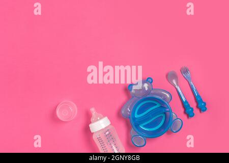 Assiette bleue sous forme d'ours, bouteille, couteau et cuillère sur table rose. Repas des enfants. Vue de dessus Banque D'Images