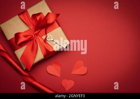 boîte carrée avec noeud en soie rouge et coeur en tissu sur fond rouge, vue du dessus, jour de la saint-valentin Banque D'Images