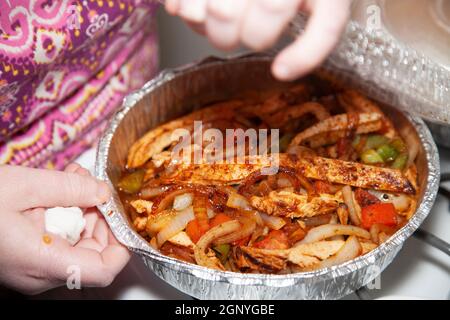 Femme ouvrant un moule à emporter de poulet sauté dans un moule de service avec des jalapenos, des poivrons verts rôtis, des oignons rôtis et du poivron rouge rôti Banque D'Images