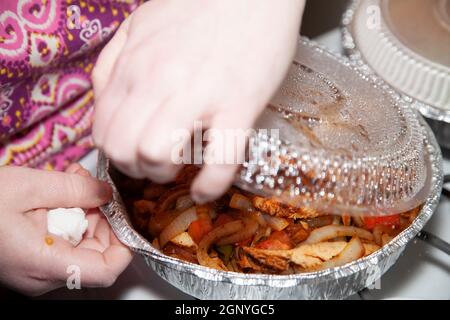 Femme ouvrant un moule à emporter de poulet sauté dans un moule de service avec des jalapenos, des poivrons verts rôtis, des oignons rôtis et du poivron rouge rôti Banque D'Images