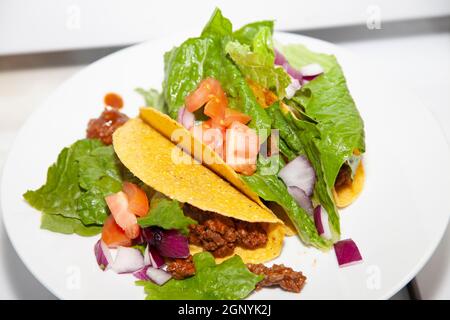 Trois tacos de bœuf haché et de salade faits avec de la laitue romaine, des tomates en dés et des oignons violets en dés sur une assiette blanche Banque D'Images