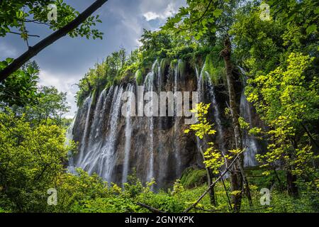 Traînées d'eau sur la grande cascade illuminée par la lumière du soleil encadrée naturellement par des branches. Parc national des lacs de Plitvice Patrimoine mondial de l'UNESCO en Croatie Banque D'Images