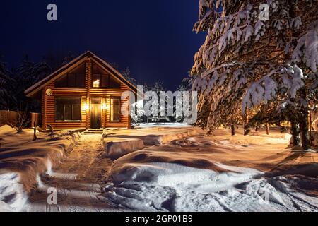 Un chemin dans la cour menant à une maison de village en rondins, pins enneigés, une fabuleuse nuit d'hiver. Paysage d'hiver rural magnifique. Location Banque D'Images