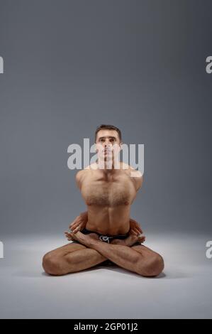 Le yoga est assis dans la posture classique, la position de méditation, l'étirement parfait, fond gris. Homme fort faisant de l'exercice yogi, entraînement à l'asana, haut de concentriti Banque D'Images