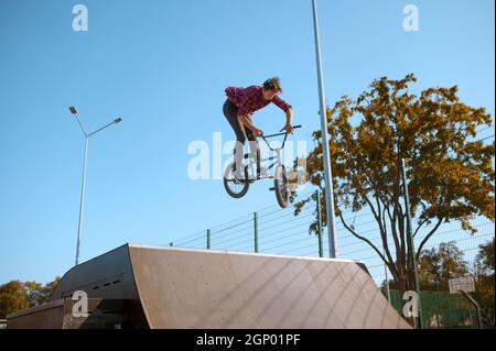 Un cycliste bmx masculin saute sur la rampe, un adolescent s'entraîne dans un skate Park. Sports extrêmes de vélo, exercice dangereux de cycle, risque de conduire dans la rue, le vélo en été Banque D'Images