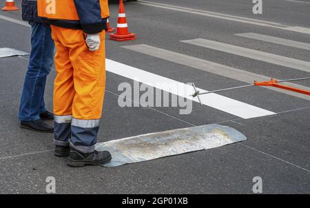 Couper les corps de deux ouvriers sur le côté de l'allée.Marquage du passage piéton sur la rue de la ville Banque D'Images