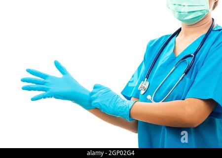 Une infirmière féminine debout avec un stéthoscope met des gants en caoutchouc et porte un masque médical, une femme médecin en uniforme bleu, prise de vue en studio isolée sur plus Banque D'Images