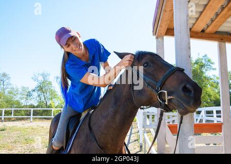 Une fille après un entraînement équestre regarde joyeusement le visage du cheval Banque D'Images