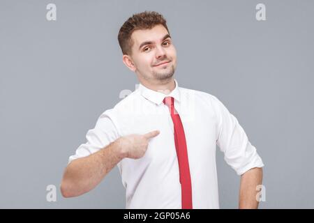 C'est moi. Portrait d'un jeune beau fier homme en chemise blanche et cravate debout, pointant et regardant l'appareil photo avec fierté visage et confiance. Intérieur isolé sur fond gris. Banque D'Images