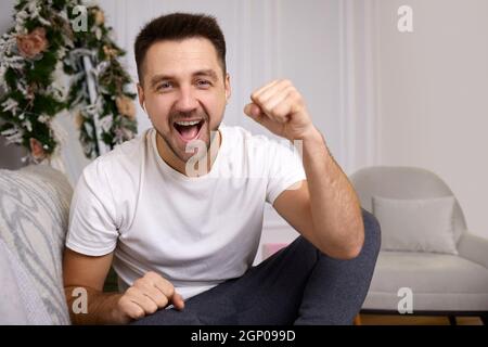 portrait du jeune homme souriant dans les écouteurs parle à quelqu'un sur appel vidéo à la maison Banque D'Images