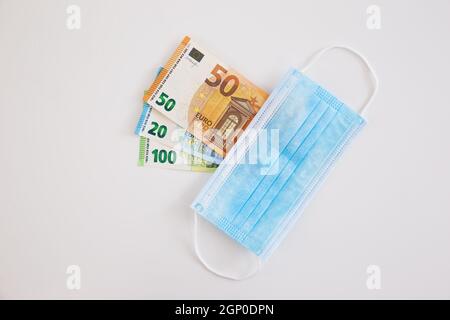 Masque chirurgical couvrant l'argent sur fond blanc. Composition de Flat Lay de billets de banque en euros cachés directement au-dessus par l'équipement médical. Concept Banque D'Images