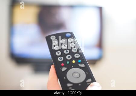 Tenez la télécommande du téléviseur dans la main, au premier plan, et le téléviseur dans l'arrière-plan flou. Diffusion en continu. Banque D'Images