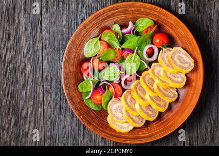 petit déjeuner au jambon et au fromage hachés petits roulés avec salade d'oignons rouges aux épinards frais sur une assiette rustique sur une table en bois, vue horizontale de Banque D'Images
