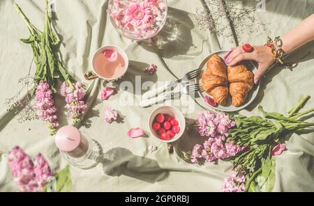 Femme tenant main croissant sur table avec nappe vert clair, fleurs roses, bougies, thé et cerises. Cadre romantique avec fleurs fraîches et Banque D'Images