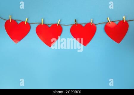 Quatre coeurs rouges accrochés au cordon fixé par des épingles dorées sur fond bleu. Symbole de l'amour sur fond coloré avec espace copie. Signe d'amour pour valenti Banque D'Images