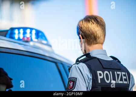 ILLUSTRATION - 28 septembre 2021, Rhénanie-du-Nord-Westphalie, Gütersloh : un policier se tient devant une voiture de patrouille avec ses feux bleus allumés. Photo: David Inderlied/dpa Banque D'Images