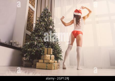 Une fille de Noël baille après le sommeil. Bâillements et étirements. Chapeau de père Noël. Charmante fille habillée de t-shirt blanc, chapeau de Père Noël et short rouge se tient à côté de Banque D'Images