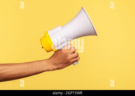 Profil vue latérale gros plan de la main humaine tenant le mégaphone, annonce de la publicité. Studio d'intérieur isolé sur fond jaune. Banque D'Images
