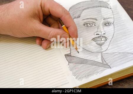 Man dessine un croquis au crayon d'un jeune homme adulte dans un journal ouvert Banque D'Images