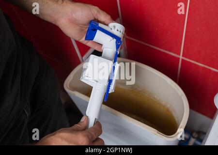 Remplacement des pièces du réservoir de toilettes. Un homme portant des gants orange répare l'évacuation du réservoir de toilettes Banque D'Images