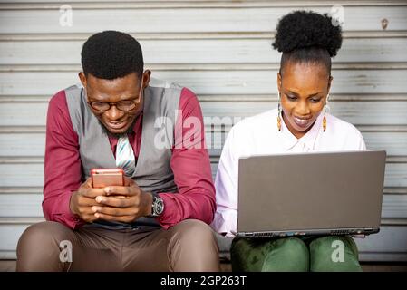 Deux hommes d'affaires africains à la recherche d'informations sur une page web de téléphone mobile, assis à une table avec un ordinateur portable et un . Collègues qui vérifient leurs e-mails sur Banque D'Images