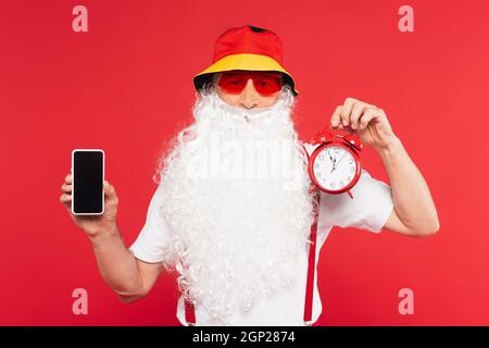 Le Père noël dans des lunettes de soleil tenant un réveil et un smartphone isolé sur le rouge Banque D'Images