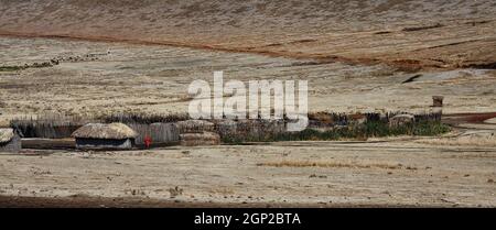 Village de Maasai, enceinte compacte, petites maisons de boue rondes, toits de chaume, clôture de l'homme, vêtements traditionnels rouges, tribu semi-nomade, terres arides, Banque D'Images