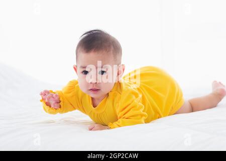 Portrait de beau jeune asiatique nouveau-né petit bébé décubitus ventral sur le lit à la maison, heureux bébé sourire porte une chemise jaune relaxant dans la chambre, Family mor Banque D'Images