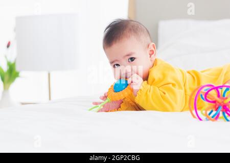 Portrait de beau jeune asiatique nouveau-né petit bébé décubitus ventral sur le lit à la maison, heureux bébé sourire porte une chemise jaune relaxant dans la chambre, Family mor Banque D'Images