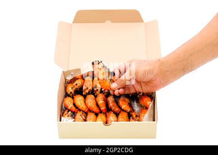 Gros plan une main humaine ramassez une crevette de rivière grillée dans une boîte de papier isolée sur fond blanc. Banque D'Images