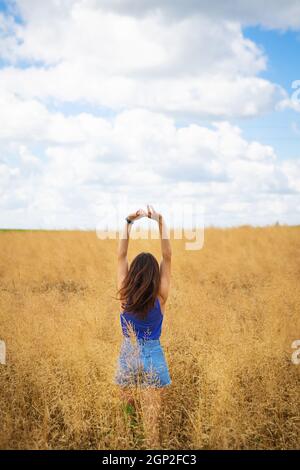 Portrait d'une jeune belle femme brune dans un t-shirt bleu et un short en denim se tient au milieu du champ, exposant son visage au soleil sur le Banque D'Images