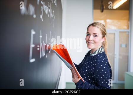 Jeune étudiant écrit sur le tableau/blackboard pendant un cours de mathématiques. Banque D'Images