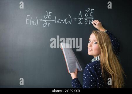 Jolie jeune étudiant écrit sur le tableau/blackboard pendant un cours de mathématiques (colort image aux couleurs peu profondes ; 6) Banque D'Images