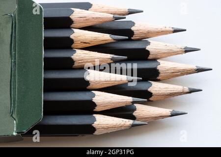 gros plan sur les pointes pointues d'un jeu de crayons graphite noirs dans un carton vert sur fond blanc Banque D'Images