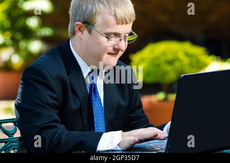 Close up portrait of businessman with down syndrome de travailler. Young man working on laptop in garden. Banque D'Images