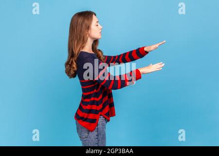 Vue latérale portrait d'une femme aveugle en chandail rayé de style décontracté, marchant seul avec les yeux fermés dans l'obscurité, se sentant désorienté, la route perdue. Studio d'intérieur isolé sur fond bleu. Banque D'Images