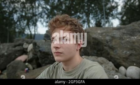 Jeune homme blond bien pensé aux yeux colorés, regardant à gauche et à droite à l'extérieur Banque D'Images