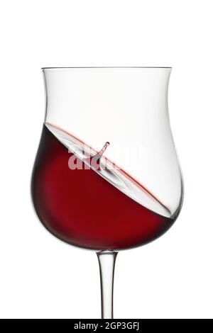 Projection dans le verre. Vin rouge en verre de vin isolé sur fond blanc. La chute tombe dans le verre et crée des éclaboussures et des vagues sur la surface du vin rouge Banque D'Images
