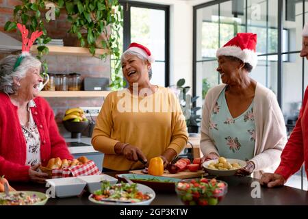 Quatre heureux divers amis de sexe masculin et féminin dans des chapeaux de noël cuisinant ensemble dans la cuisine Banque D'Images