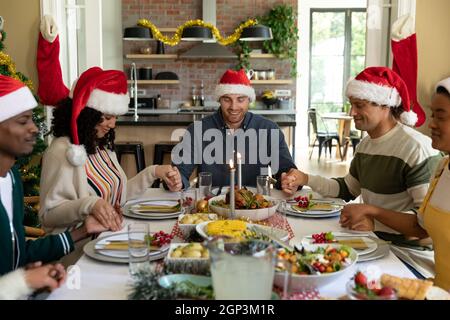 Groupe d'amis de sexe féminin et masculin heureux et variés prenant un repas de noël, priant ensemble à la maison Banque D'Images